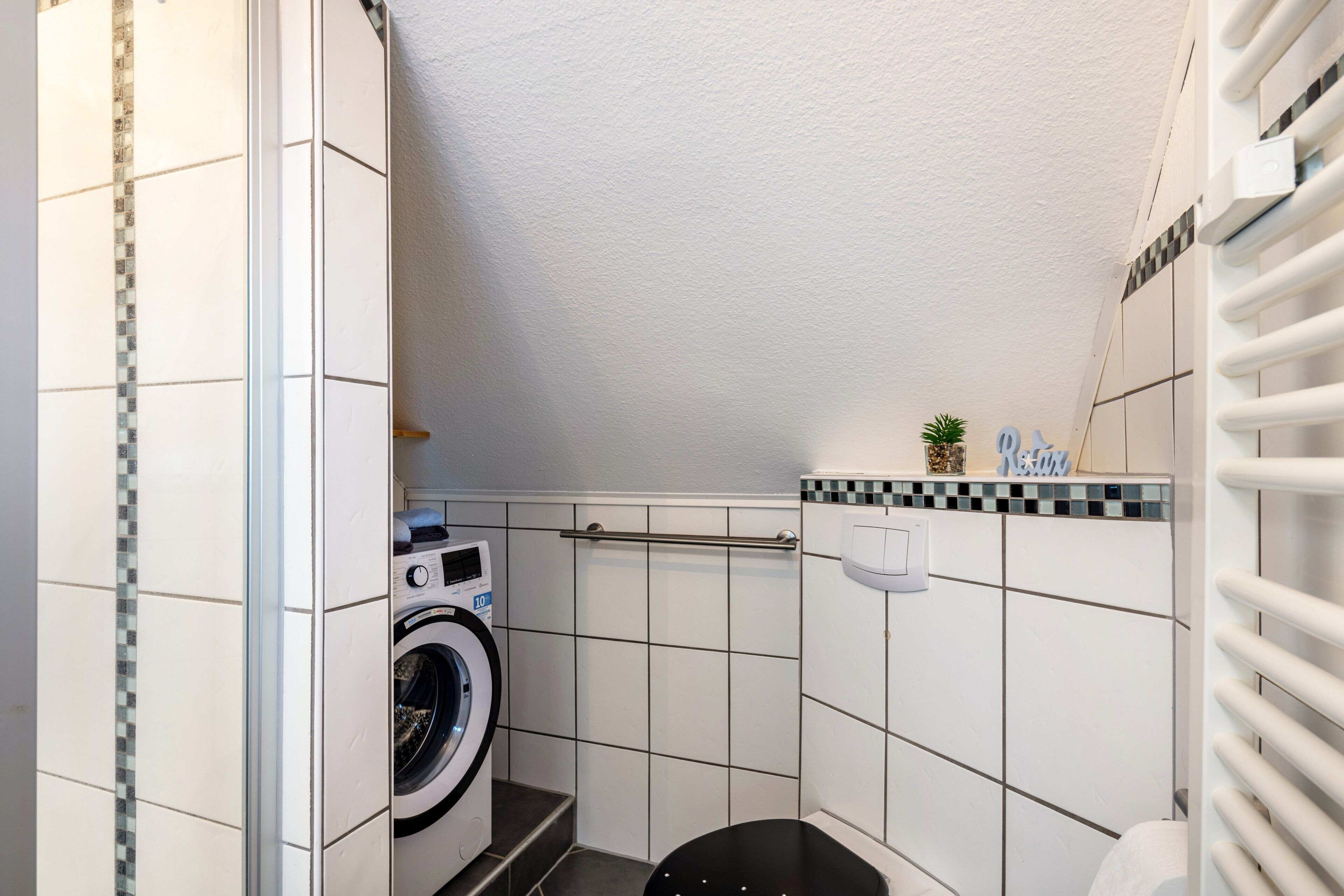 A compact bathroom with a washing machine, a toilet, and a towel rack.
