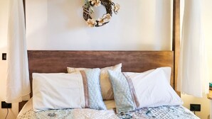 A neatly made bed with a floral-patterned bedspread and pillows, a wooden headboard, and a decorative wreath hanging above. - La Vigna di Ranco Agriturismo (Paglieta)
