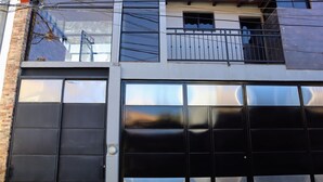 Fachada de edificio con grandes puertas de garaje, pared de ladrillo y balcón con barandilla de metal.