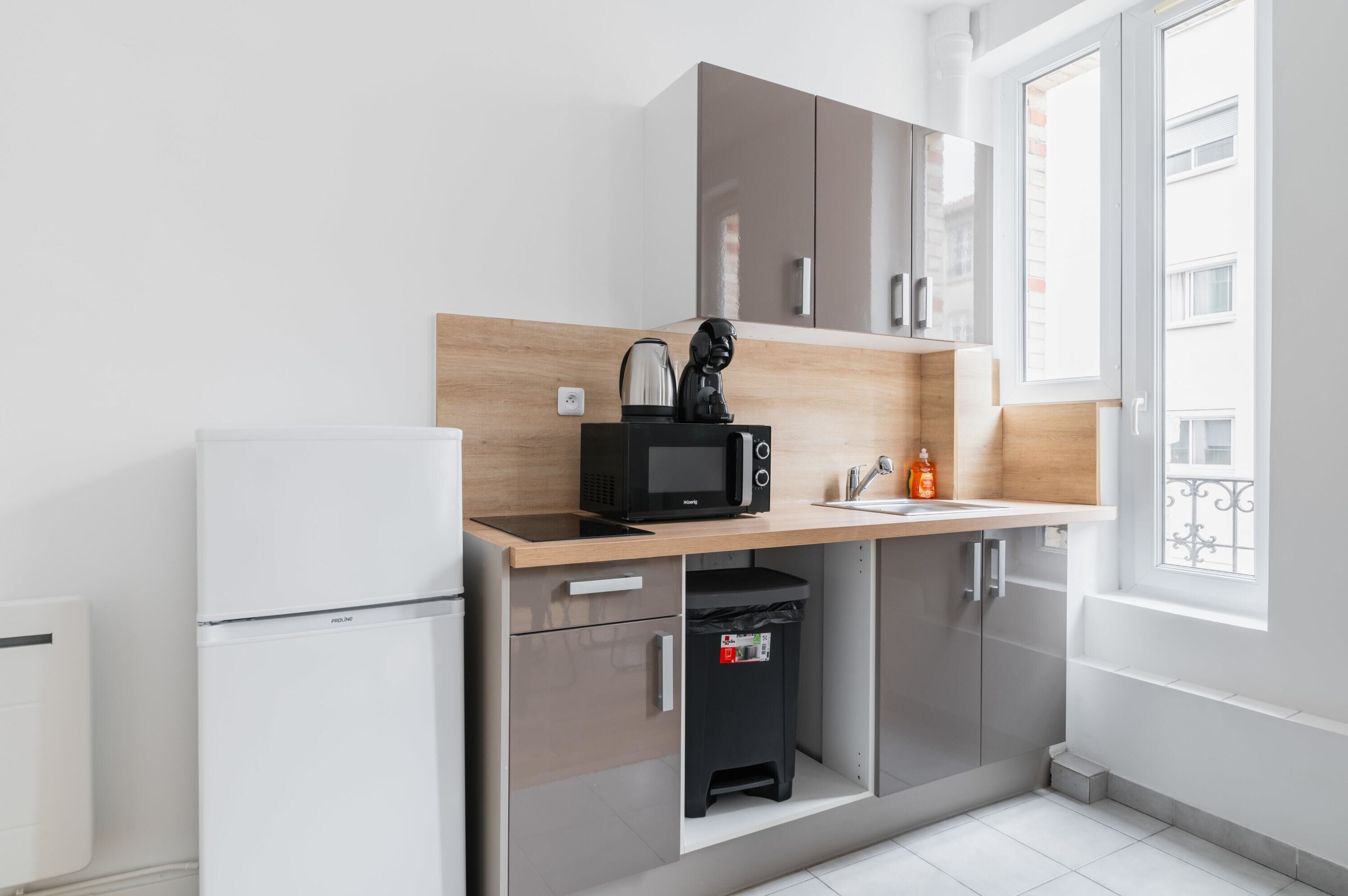 A modern kitchen with a built-in microwave, a kettle, and a small trash bin.