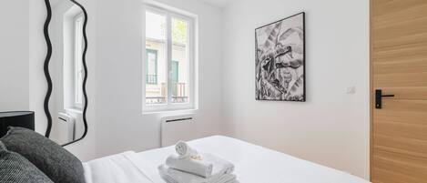 Una habitación de hotel con una cama, una ventana, una puerta y una obra de arte colgada en la pared.