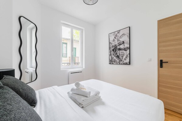 A hotel room with a bed, a window, a door, and a wall-mounted artwork.