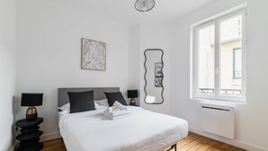 A hotel room with a bed, bedside lamps, a wall-mounted mirror, a window with a view, and a framed artwork. - Modern 60m² Apartment Near Metro - Paris 12 (Paris)