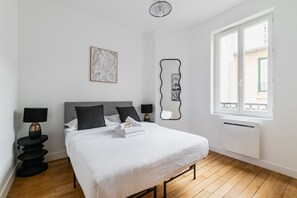 Une chambre d’hôtel comprenant un lit, des lampes de chevet, un miroir fixé au mur, une fenêtre avec vue et un tableau encadré.