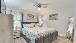 Une chambre à coucher avec un lit, des tables de chevet, un ventilateur de plafond et des œuvres d’art accrochées aux murs.