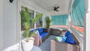 Une véranda couverte, aménagée avec des meubles en osier, des plantes en pot et un ventilateur de plafond.