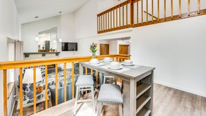 Ein Essbereich mit einem Holztisch, gedeckt für vier Personen, eine Treppe mit hölzernen Geländern und eine Küche im Hintergrund.