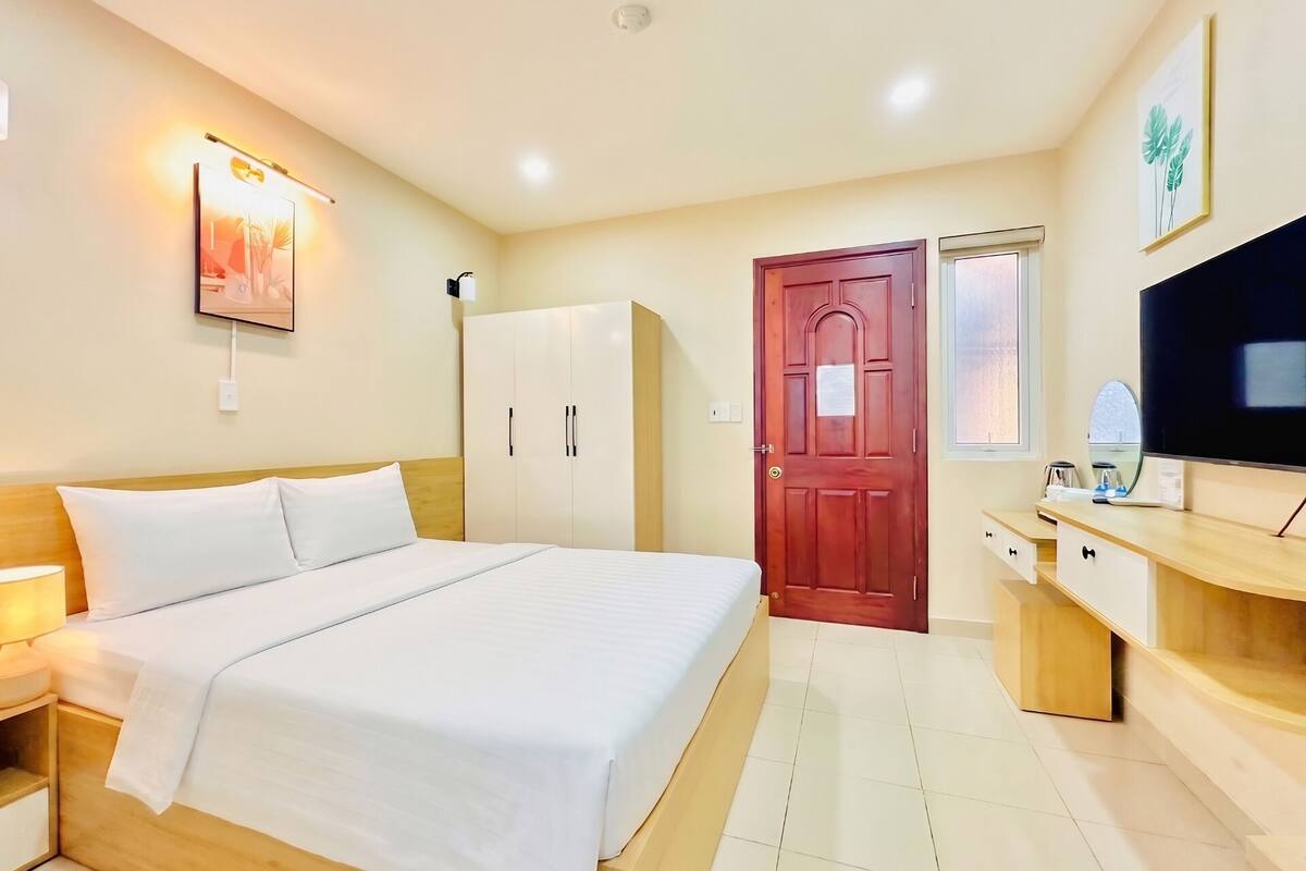 Habitación de hotel con cama, armario, televisor y escritorio con espejo.