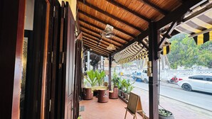 Uma área externa coberta com teto de madeira, plantas em vasos e uma cadeira.