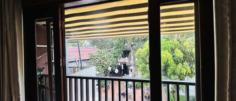 Una habitación con vistas a un patio, que incluye un balcón de madera con toldo a rayas, suelo de piedra y un edificio de techo rojo al fondo.