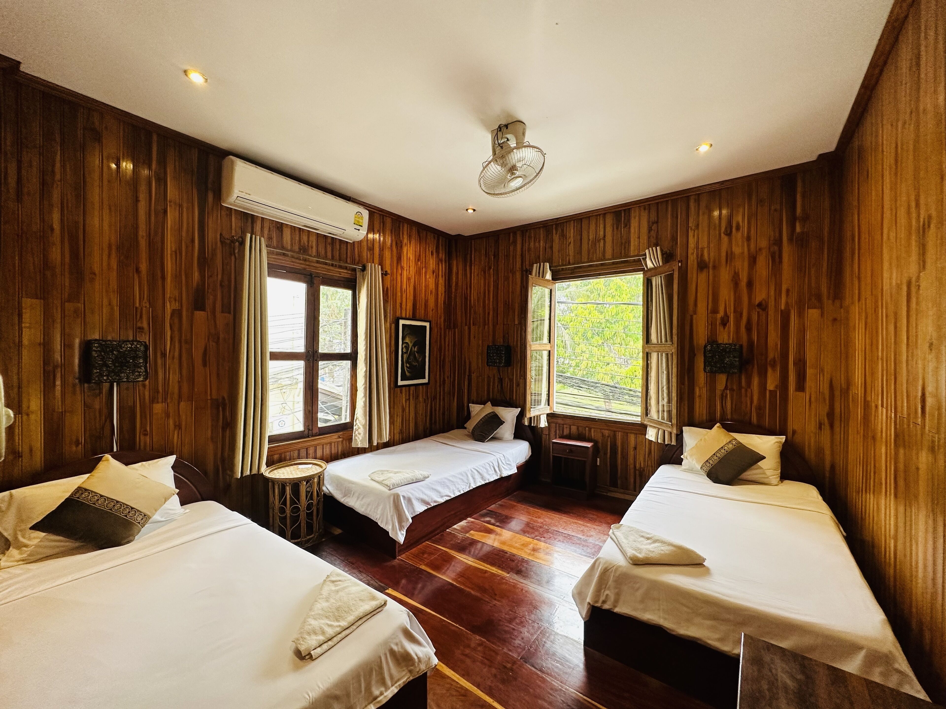 A room with wooden walls, two beds, a small table, and a ceiling fan.