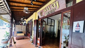 Uma pensão com fachada de madeira, entrada coberta por azulejos e uma placa com informações de contato.