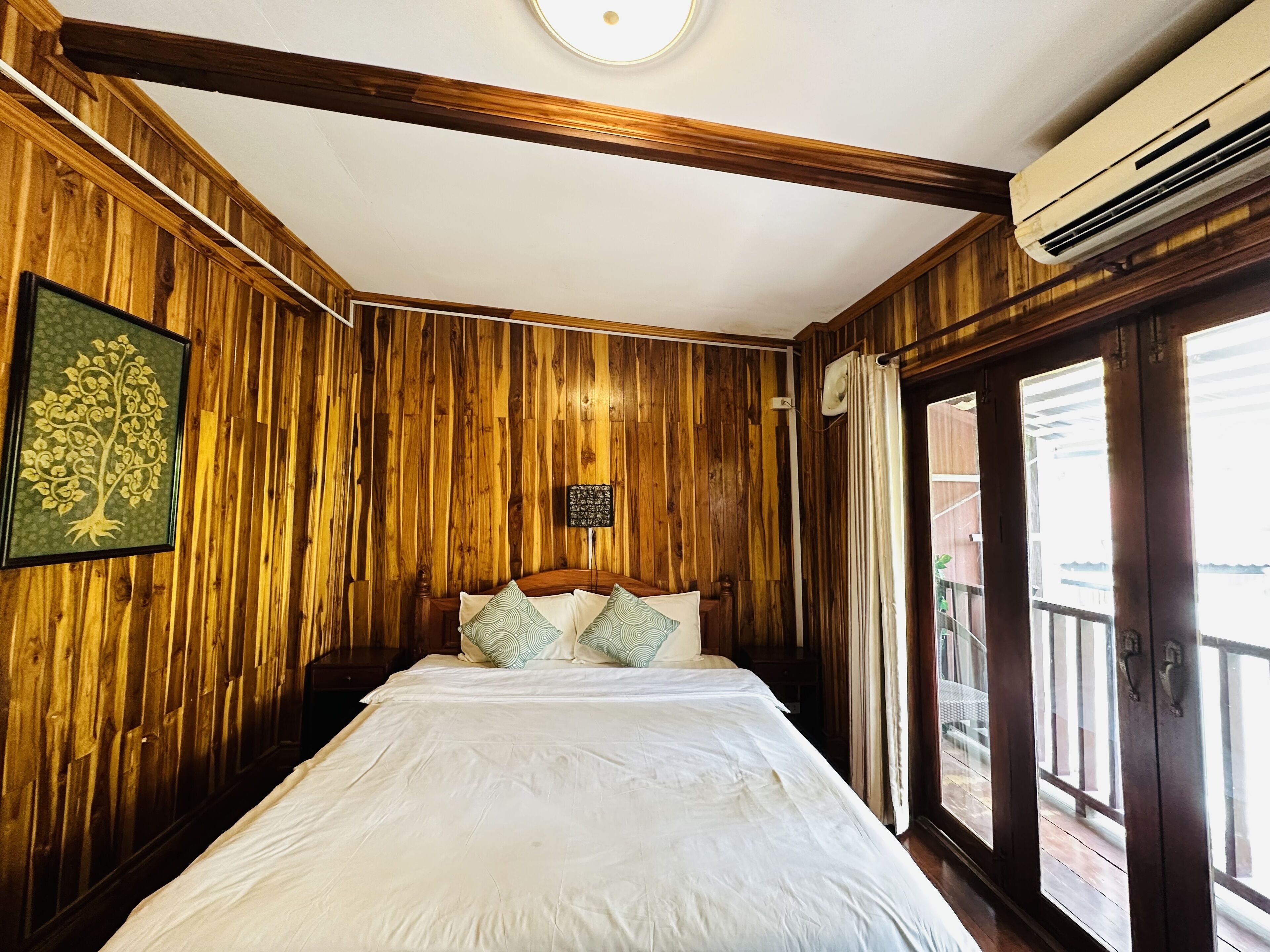 A room with wooden panel walls, a bed with white bedding, a framed picture, and a window with curtains.