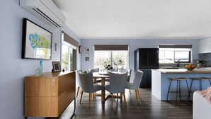 A modern kitchen with a dining area, featuring a wooden dining table, grey chairs, and a kitchen island with stools.