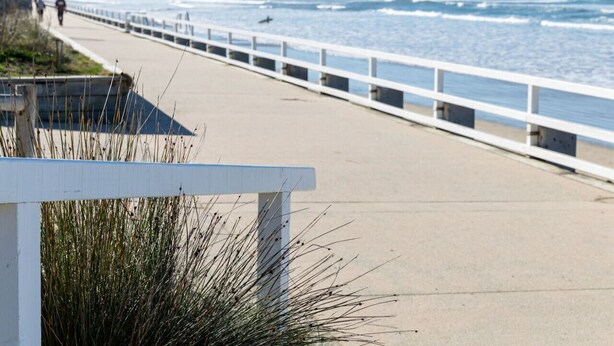 A coastal walkway with a white railing, leading to the ocean.