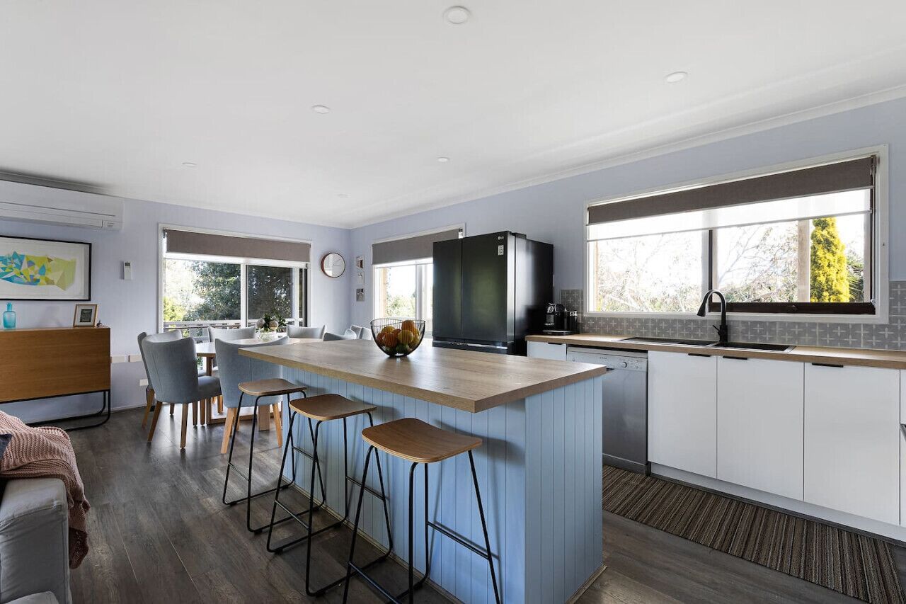 A modern kitchen with a central island, bar stools, a refrigerator, and a dishwasher.