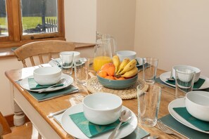 A breakfast table set with bowls, plates, glasses, a pitcher of orange juice, and a bowl of fruit. - Beautiful Cottage in Idyllic Somerset Countryside (Shepton Mallet)