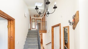A staircase with a wooden handrail, a black chandelier, and a wooden door on the right.