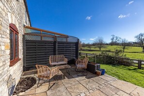 A patio with wicker furniture, a stone wall, and a view of a green field. - Beautiful Cottage in Idyllic Somerset Countryside (Shepton Mallet)