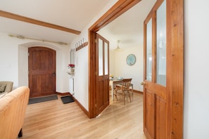 A wooden door leading to a dining area with a table and chairs, a clock on the wall, and a wooden bench in the foreground. - Beautiful Cottage in Idyllic Somerset Countryside (Shepton Mallet)