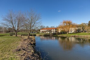 Vista sul fiume con un edificio in pietra, un molo di legno e un terreno erboso.