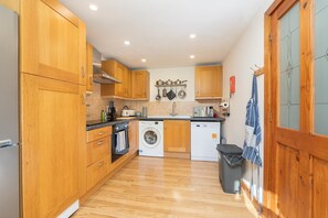 A compact kitchen with wooden cabinets, a washing machine, and a dishwasher. - Beautiful Cottage in Idyllic Somerset Countryside (Shepton Mallet)