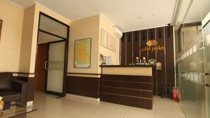 Zona de recepción de hotel con un separador de vidrio, un mostrador de recepción, un sofá y un mapa en la pared.