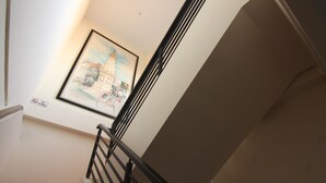 Una escalera con barandal negro, un cuadro enmarcado de un edificio en la pared y un cartel de 'No Fumar'.