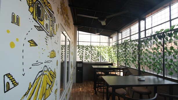 Un interior moderno con suelo de madera, una zona de comedor con mesas y sillas, y una pared decorada con plantas verdes.
