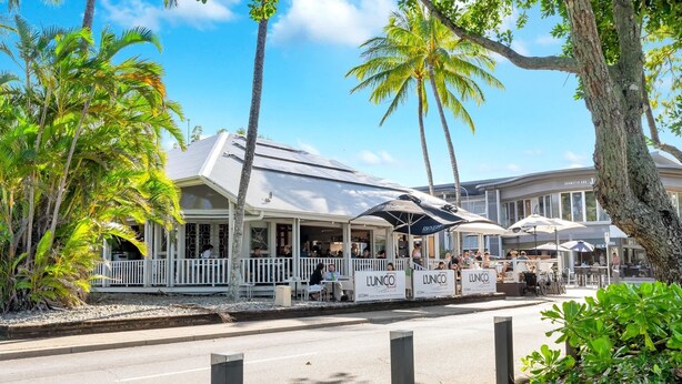 A beachfront hotel with outdoor seating, palm trees, and a clear sky. - Beachfront 3-Bed with Pool & Stunning Ocean Views (Trinity Beach)