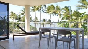 A balcony with a table and chairs, a ceiling fan, and a view of palm trees. - Beachfront 3-Bed with Pool & Stunning Ocean Views (Trinity Beach)