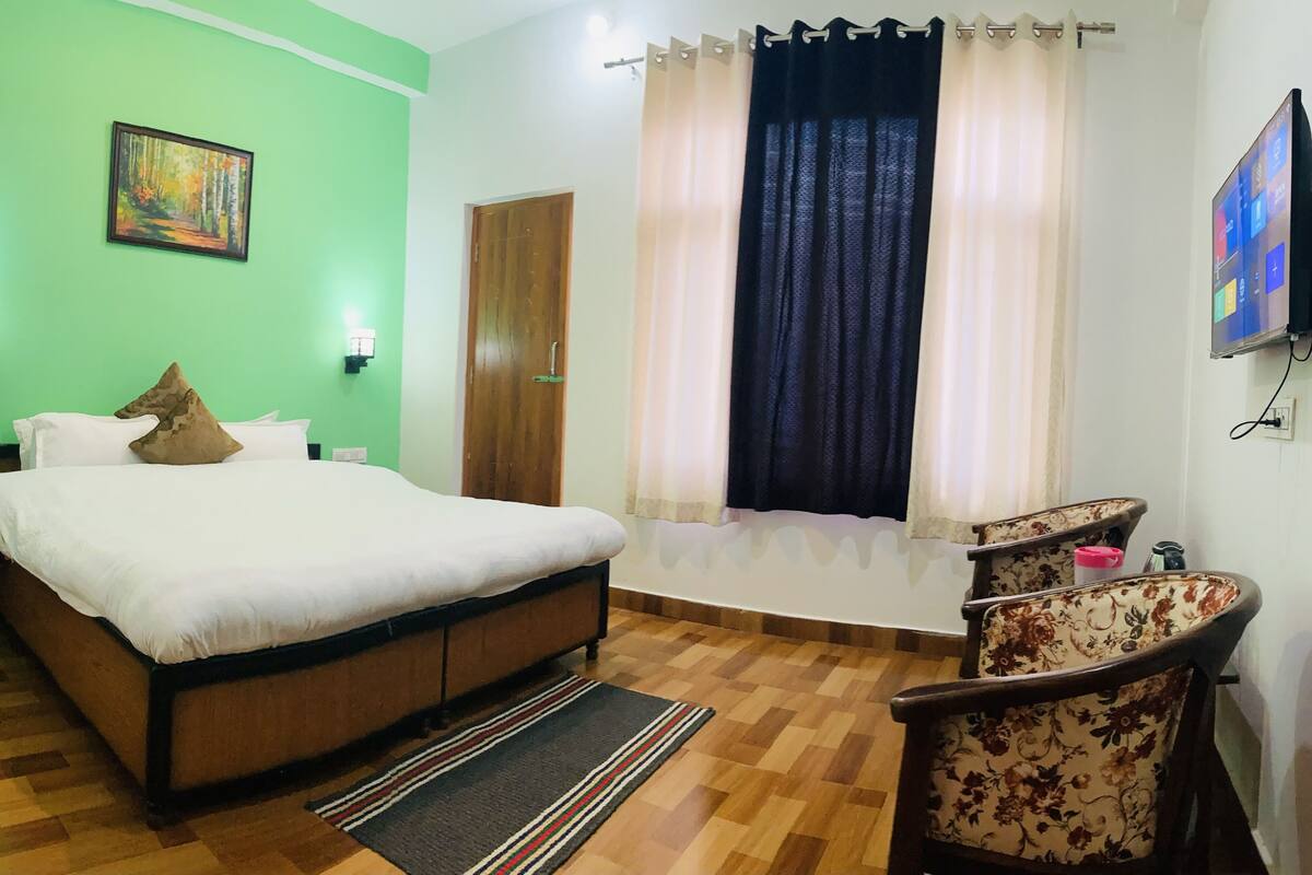 A room with a bed, a chair, a painting, a window with curtains, and a television.