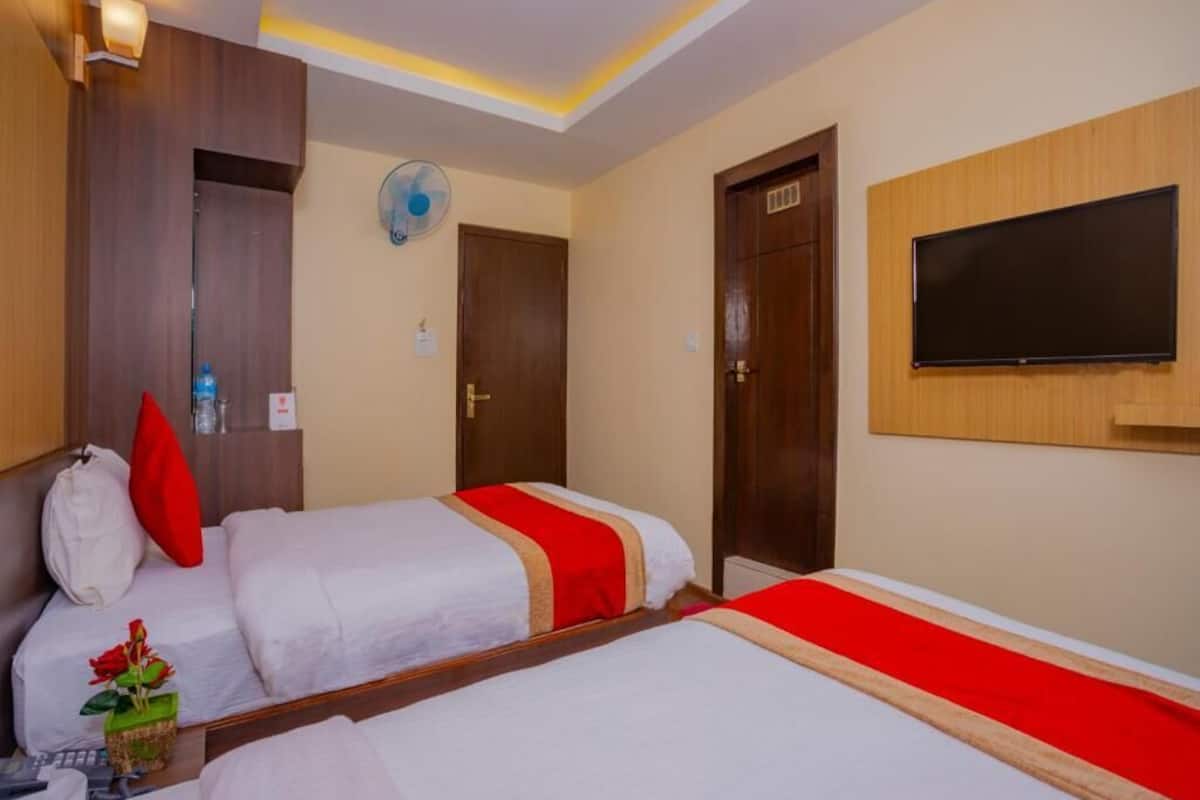 Ein Hotelzimmer mit zwei Betten, einem Fernseher, einem Ventilator und einem Holzschrank.
