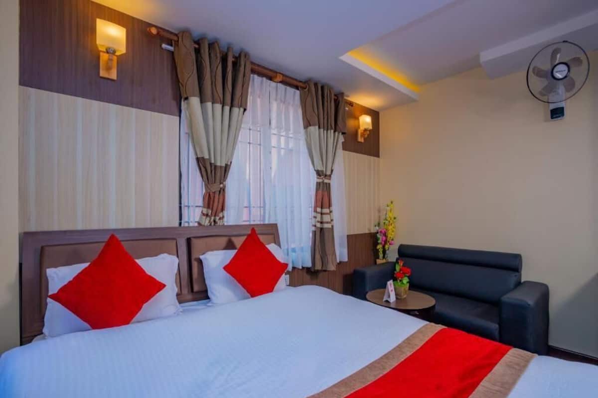 Ein Hotelzimmer mit einem großen Bett, zwei roten Kissen, einem Nachttisch mit Blumen und einem Wandventilator.