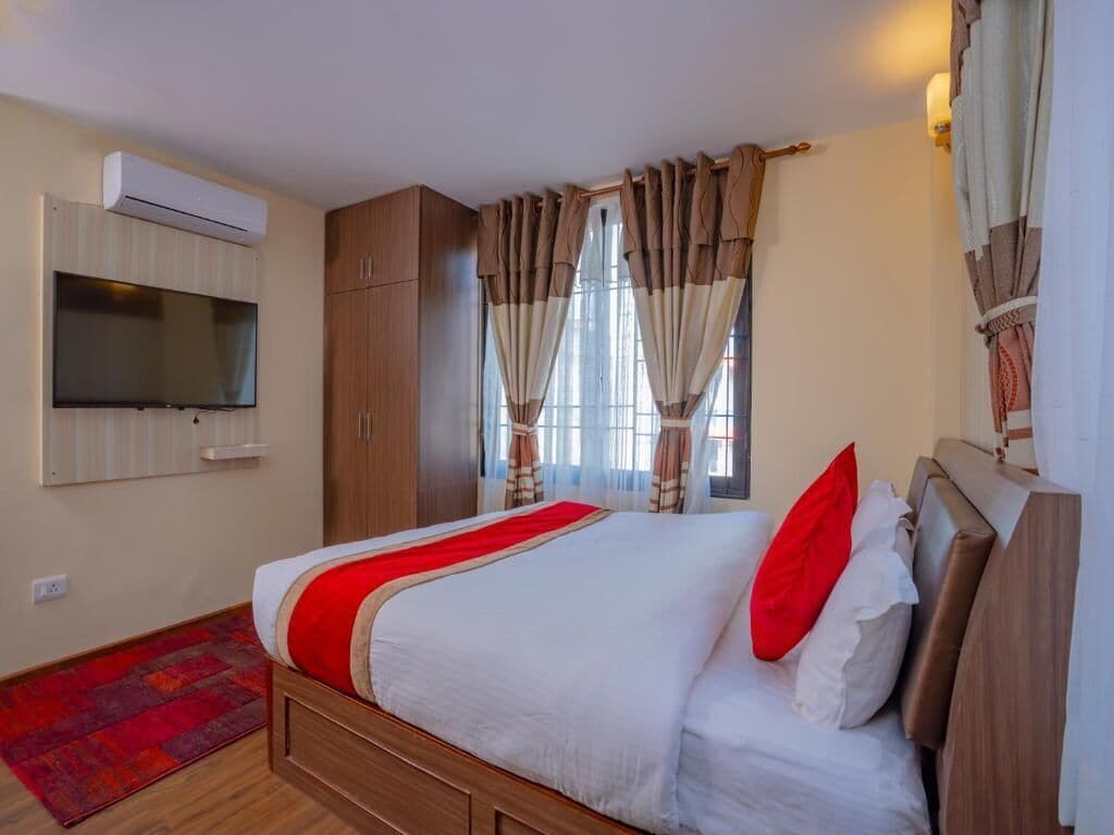 A bedroom with a bed, curtains, an air conditioning unit, and a television.