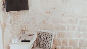 Une pièce avec un mur en pierre, un téléviseur à écran plat fixé au mur, une petite table avec une télécommande, un verre et un coussin à motifs.