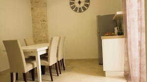 Un coin repas avec une table et des chaises blanches, un mur d’accent en pierre, une horloge, et un espace cuisine comprenant un réfrigérateur et un évier.