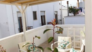 Un balcon agrémenté de meubles blancs, notamment des chaises et une table, ainsi que d’une plante en pot.