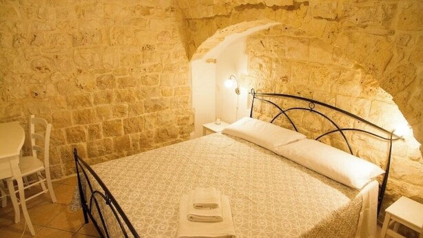 Une pièce avec un mur en pierre, un lit recouvert d’une courtepointe à motifs, une table de chevet avec une lampe et une chaise.