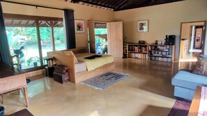 A spacious living area with a large bed, a sofa, a bookshelf, and a dining table. - Private nature estate near Mt Merapi, Yogyakarta, stylish villa 4/6 persons (Kabupaten Sleman)