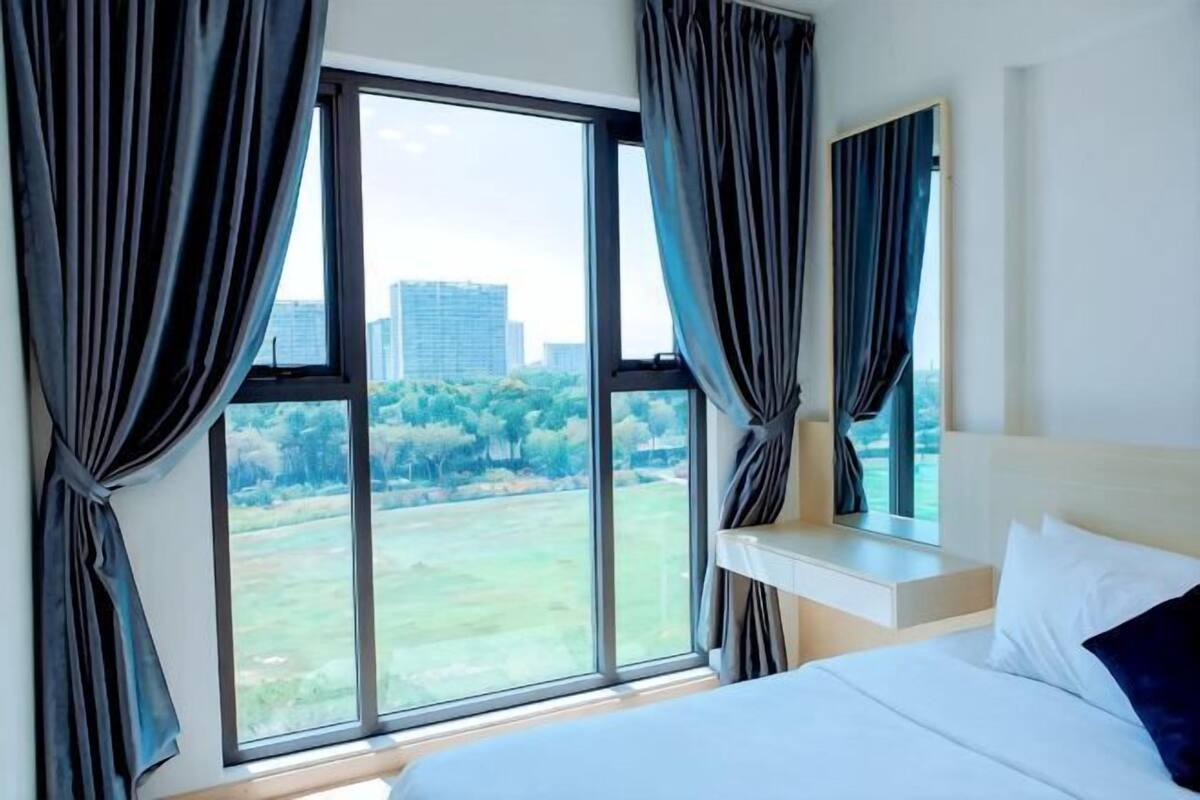 Hotelkamer met een groot raam, een bed, een nachtkastje en uitzicht op een park en gebouwen.