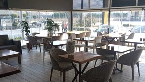 A spacious indoor seating area with tables and chairs, large windows offering a view of the street outside. - Seda Park Otel (Biga)
