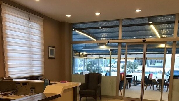 A modern reception area with a reception desk, a chair, and a view of the outdoor seating area through glass doors. - Seda Park Otel (Biga)