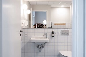 A bathroom with a white sink, mirror, and toilet. There are toiletries on the sink and a towel rack above the mirror. - South Studios 2BR by Daniel & Jacob's (København)