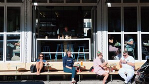 Una cafetería con terraza, grandes ventanales y un interior visible con mesas y sillas.