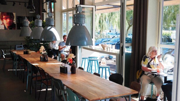 Un restaurante con una larga mesa de madera, taburetes de bar azules y lámparas colgantes.