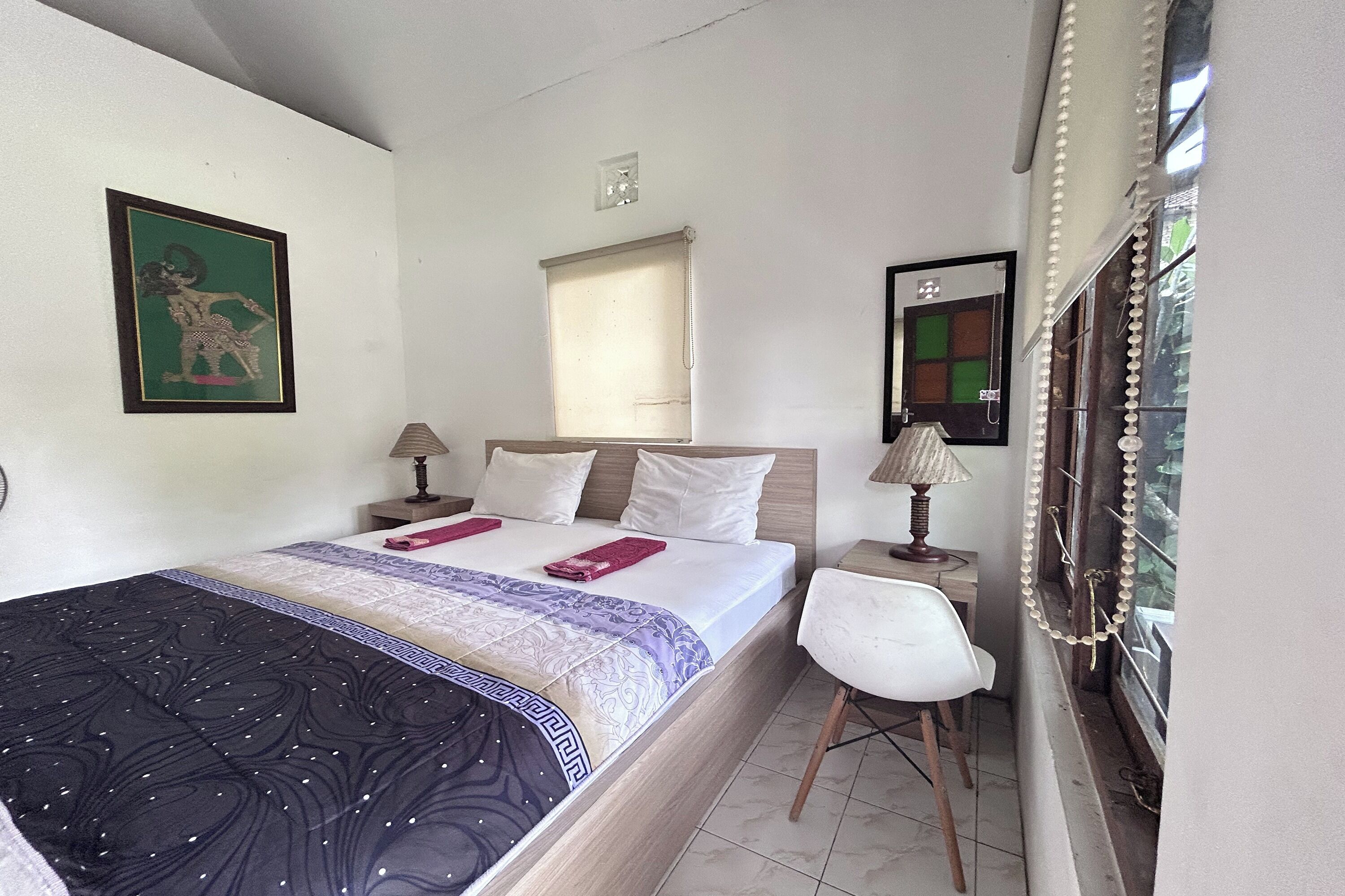 Una camera d'albergo con un letto, due comodini con lampade, una sedia, una finestra con tende e uno specchio fissato alla parete.