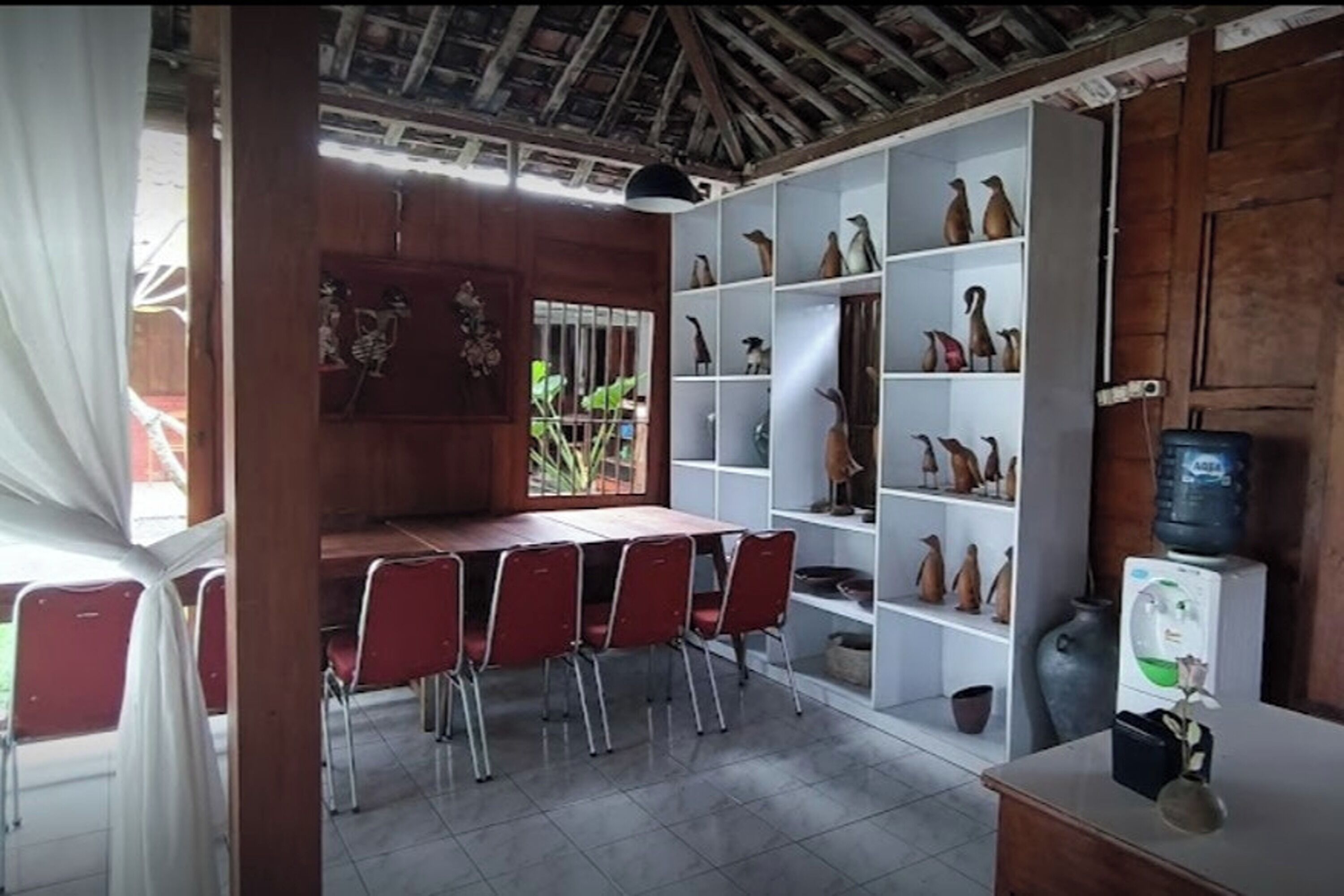 A dining area with a wooden table and red chairs, surrounded by white shelves with decorative items.