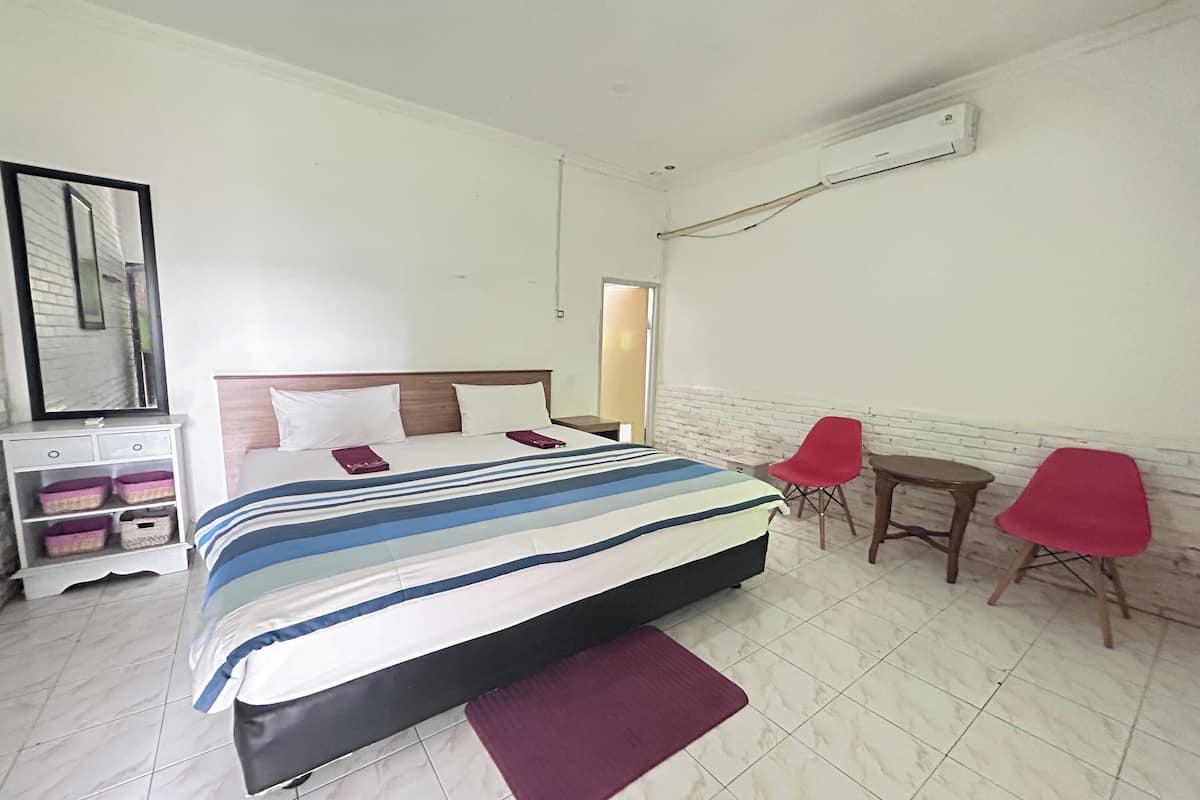 A hotel room with a bed, a nightstand, a chair, a small table, and a wall-mounted air conditioner.