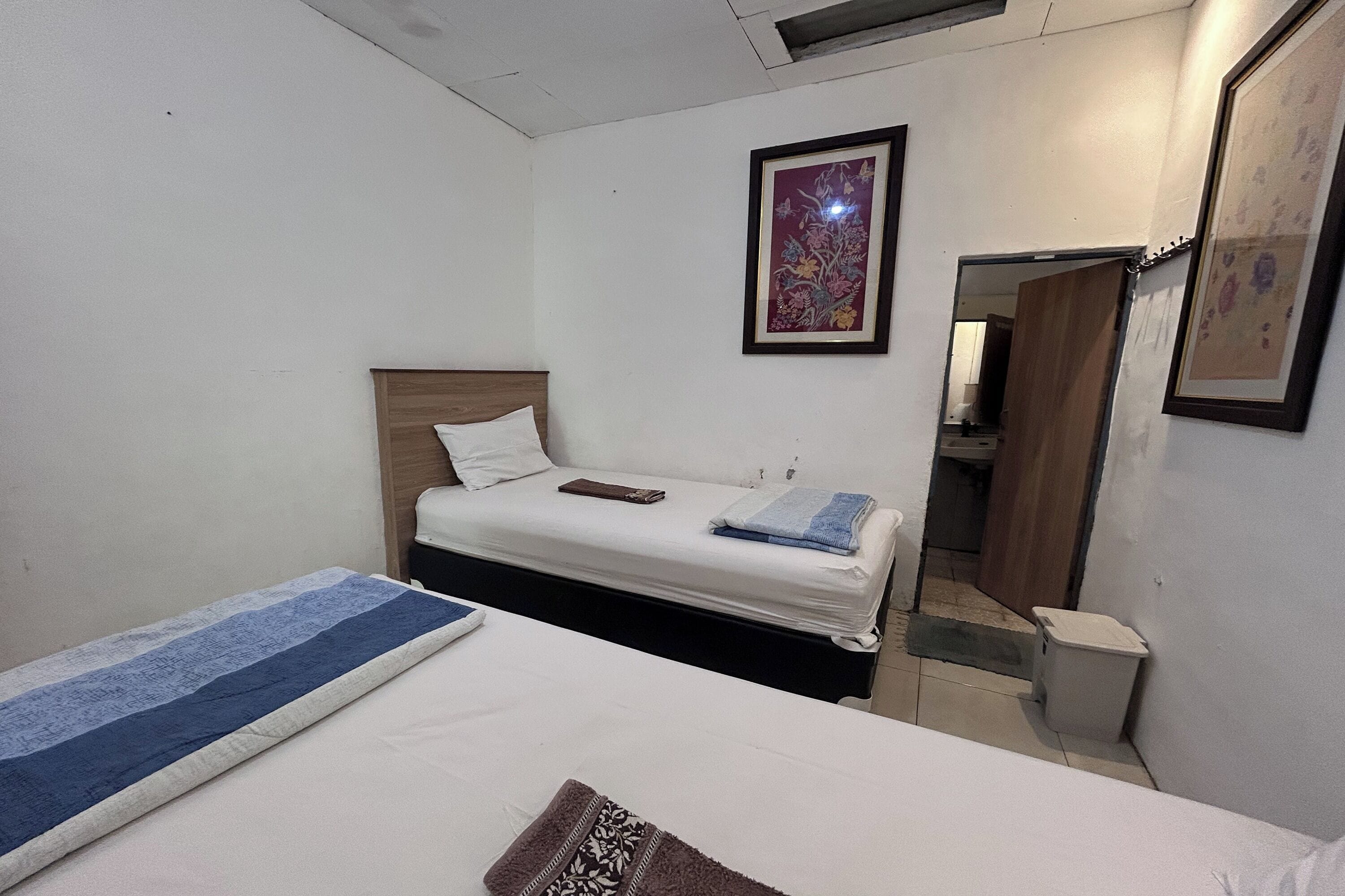 A small, clean room with a single bed, a bedside table, and a framed picture on the wall.